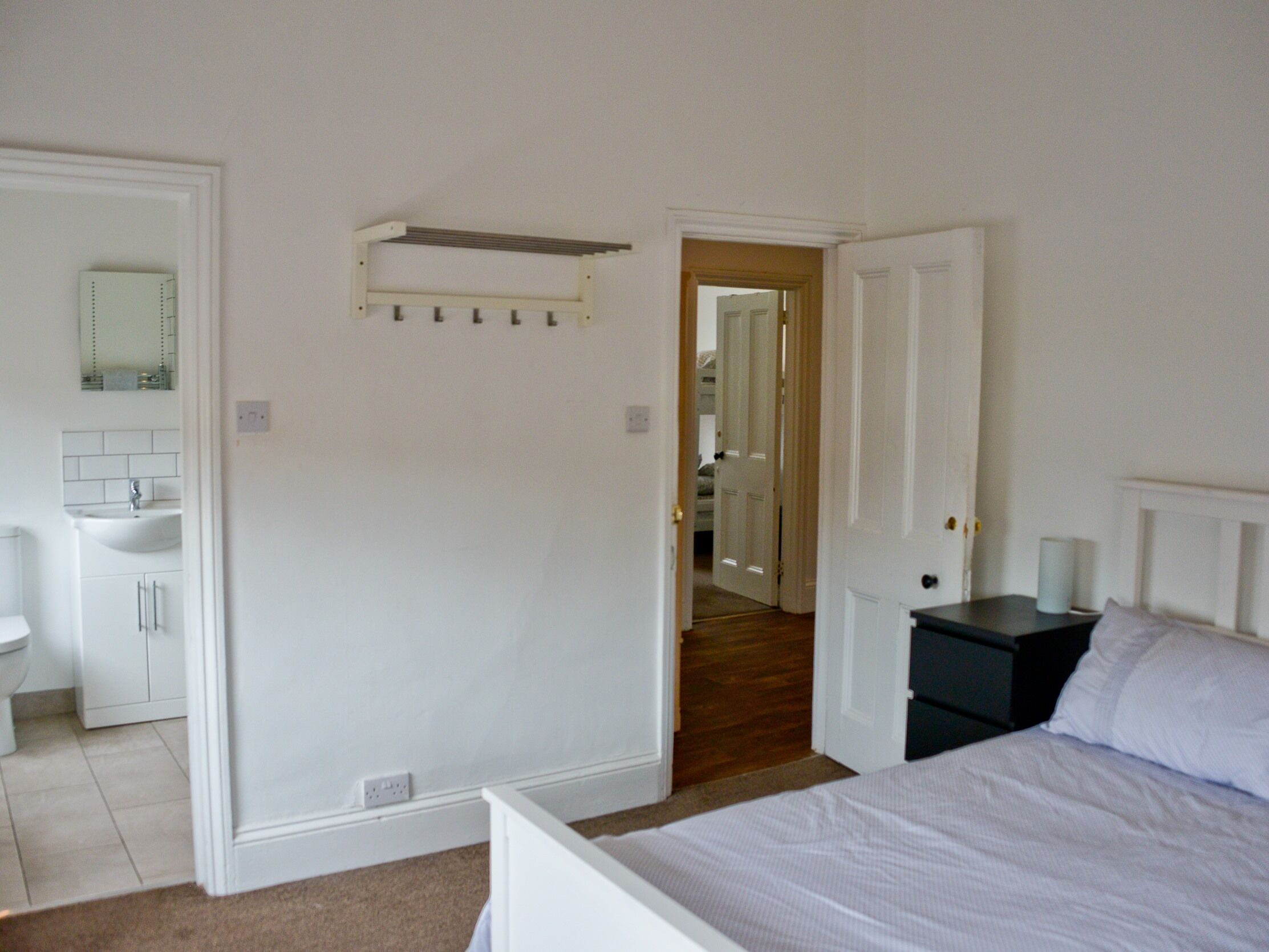 A bedroom with a bed, a nightstand, a dresser, and a bathroom with a sink and mirror.