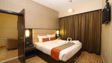 A hotel room with a bed, a nightstand, a lamp, a television, and a door.