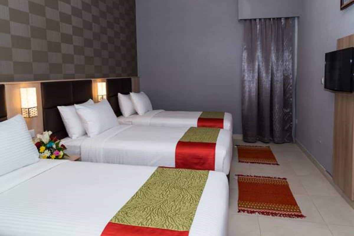 Quarto de hotel com duas camas, parede quadriculada, televisão de tela plana e janela com cortinas.