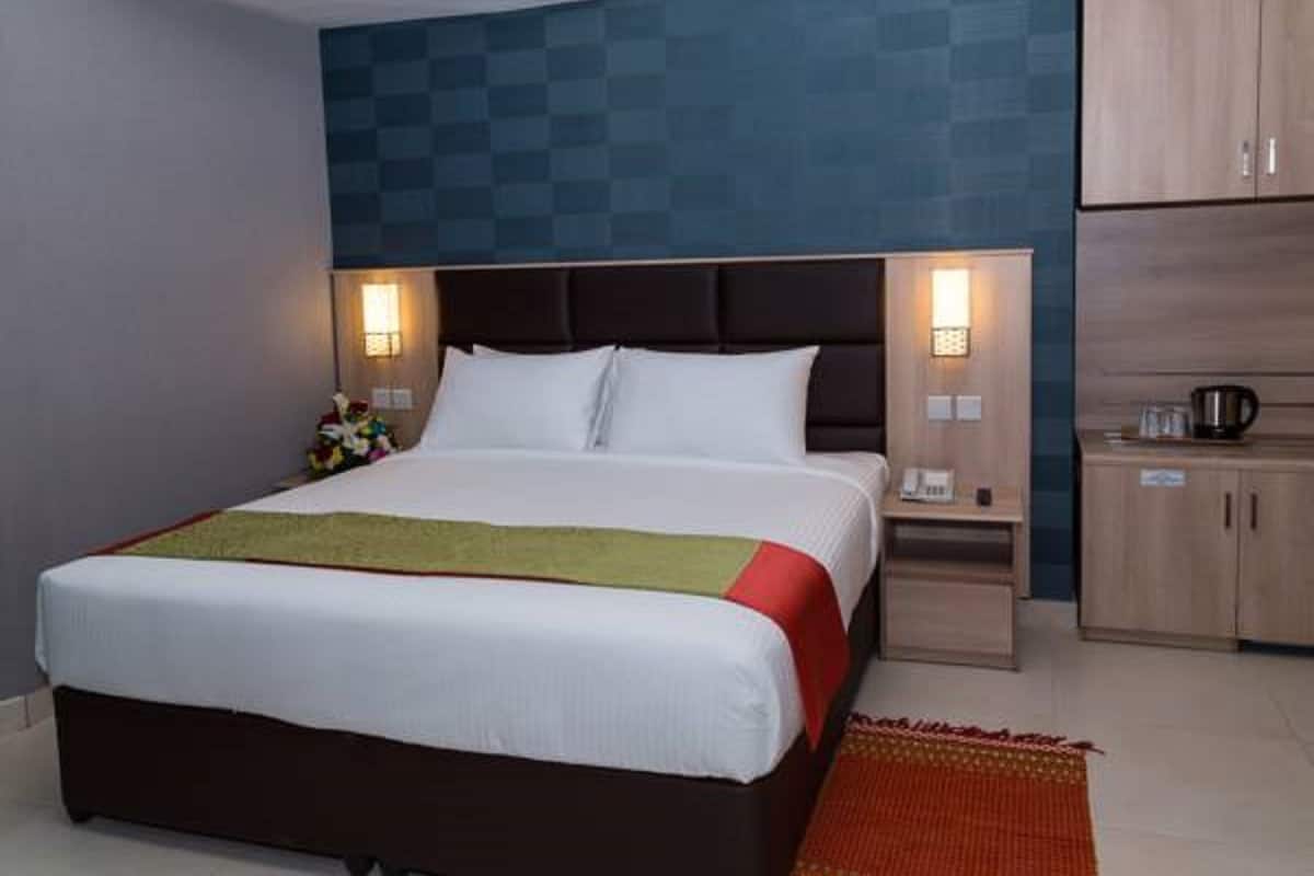 Quarto de hotel com cama grande, mesas de cabeceira, um criado-mudo e guarda-roupa.