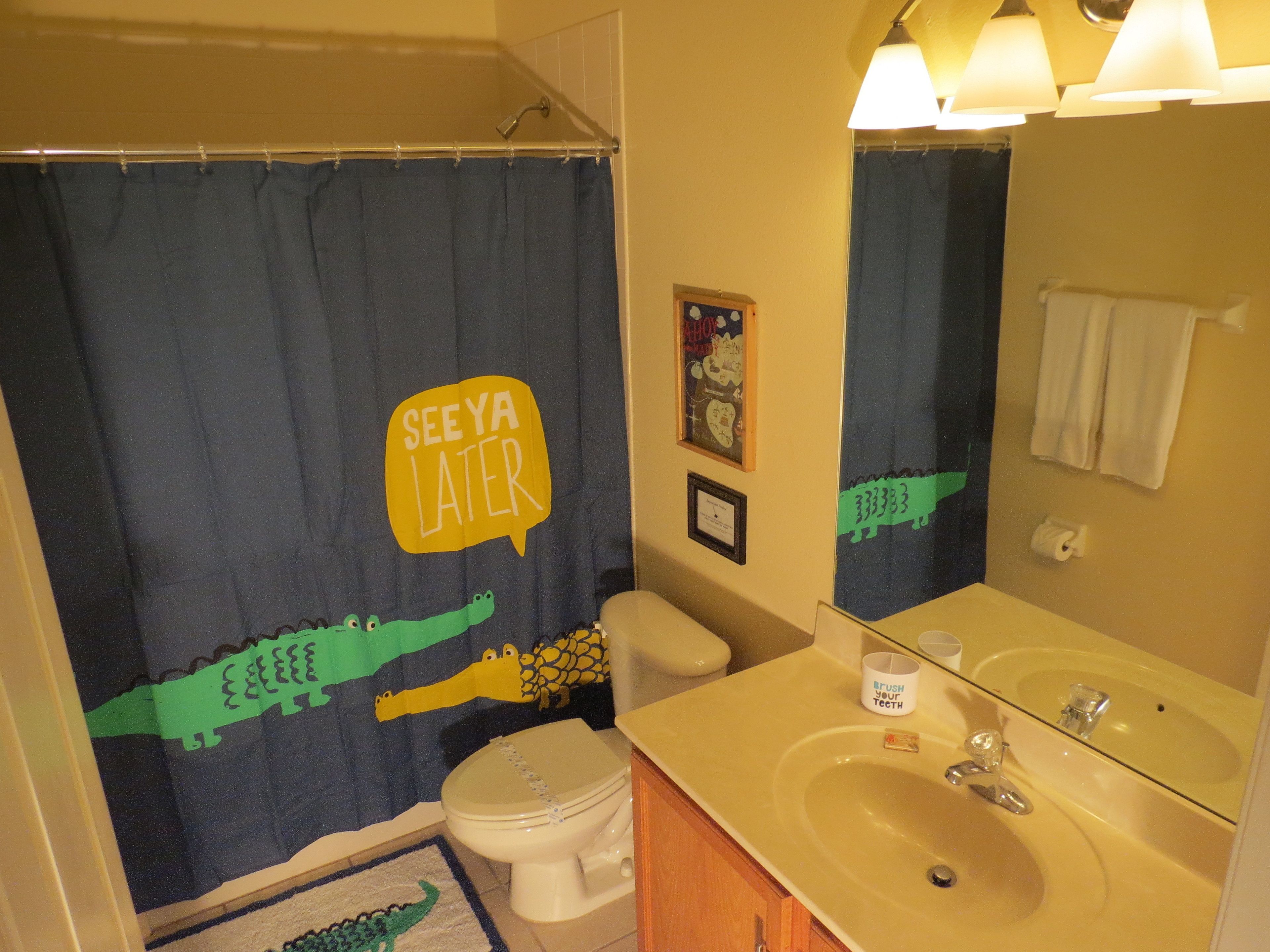 A bathroom with a shower curtain featuring a crocodile design and the text "SEE YA LATER".