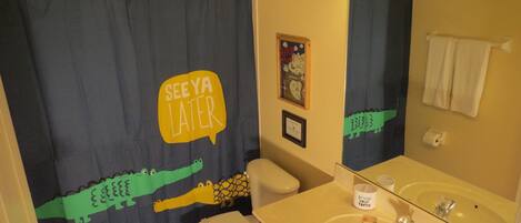Une salle de bain avec un rideau de douche orné d’un motif de crocodile et portant l’inscription « À BIENTÔT ».