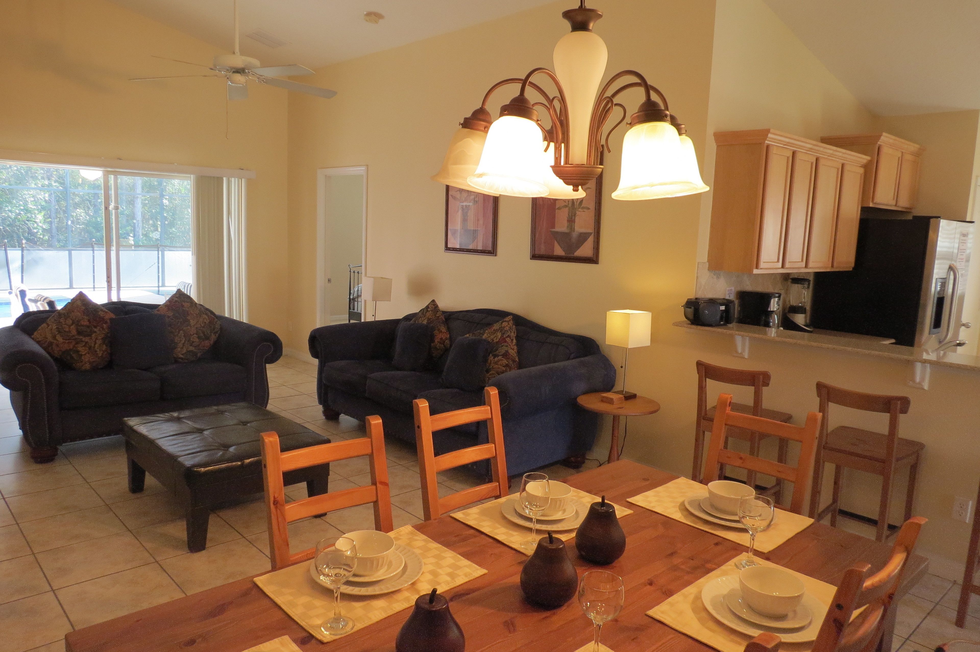 Una sala de estar con dos sofás, una mesa de centro y una mesa de comedor para cuatro personas. Incluye una zona de cocina con armarios y un refrigerador.