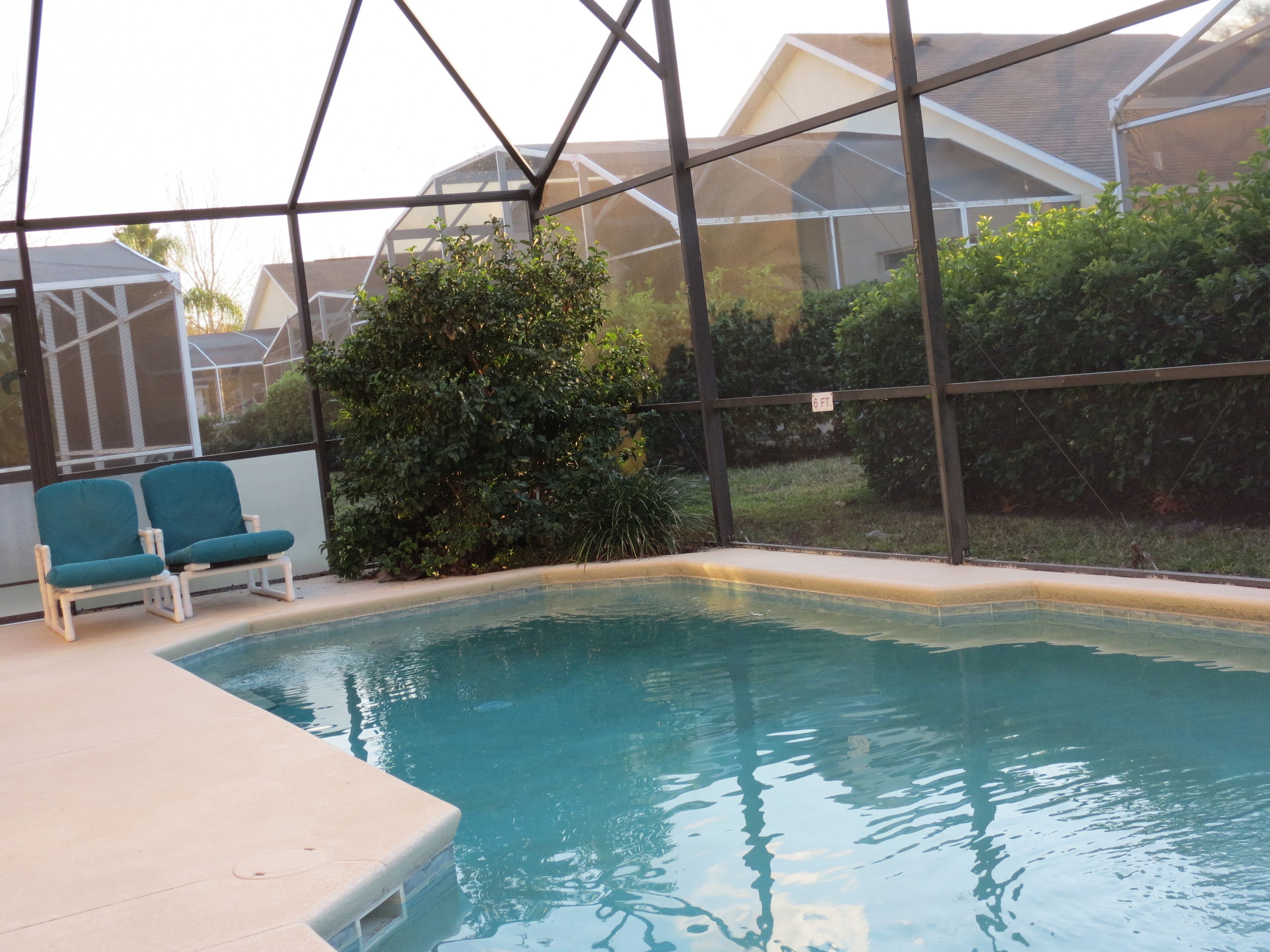 Piscina interior com água azul cristalina, cercada por uma estrutura de vidro. Dois espreguiçadeiras azuis estão localizadas à esquerda da piscina.
