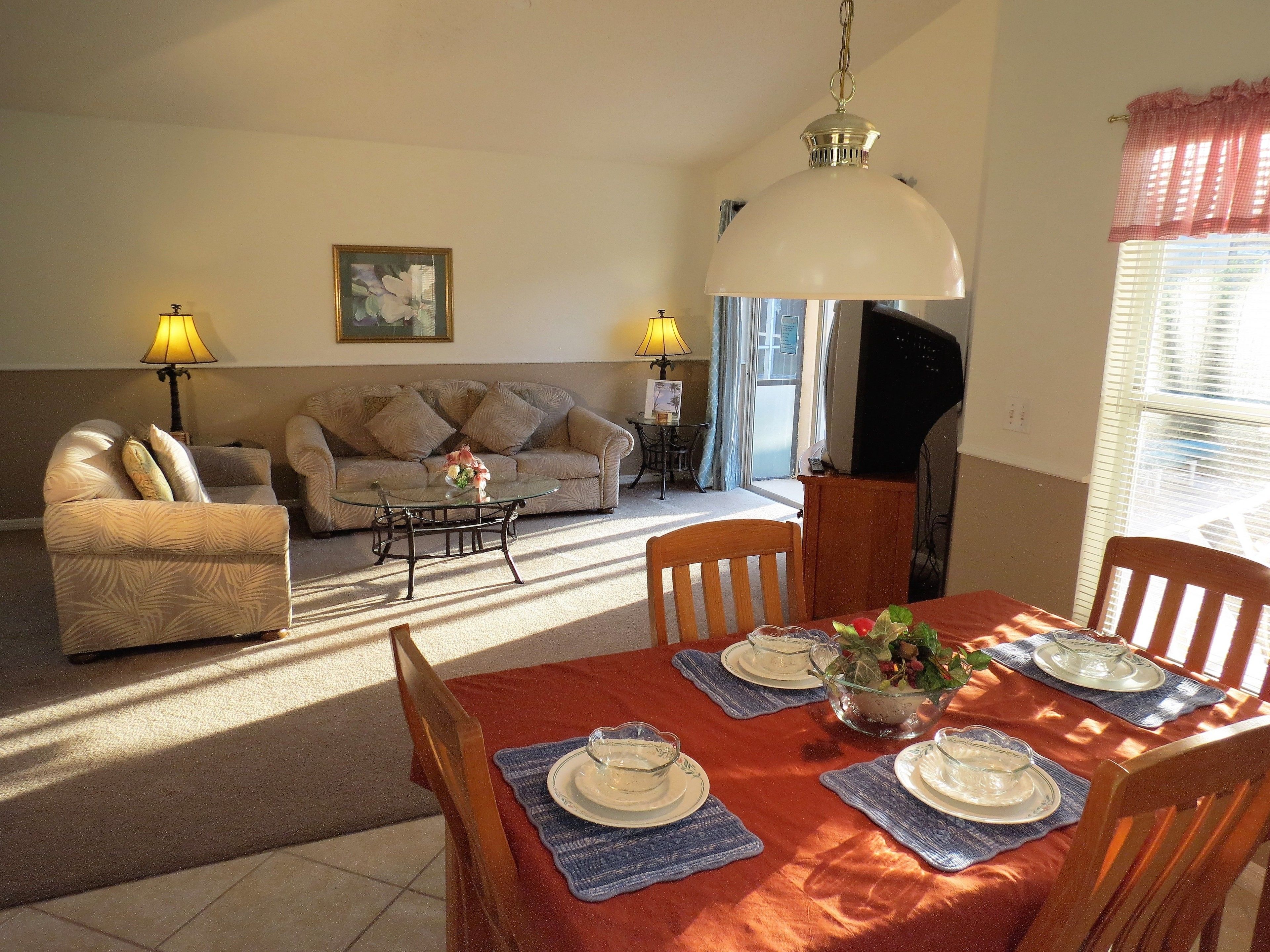 A dining area with a table set for four, a sofa, and two lamps.
