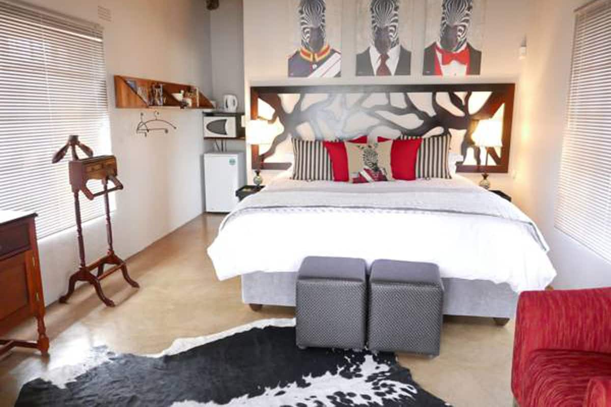 A bedroom with a large bed, a wooden nightstand, a red chair, a cowhide rug, and zebra-themed artwork on the wall.