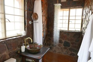 Un baño rústico con pared de piedra, lavamanos de madera, espejo y ducha con cortina.