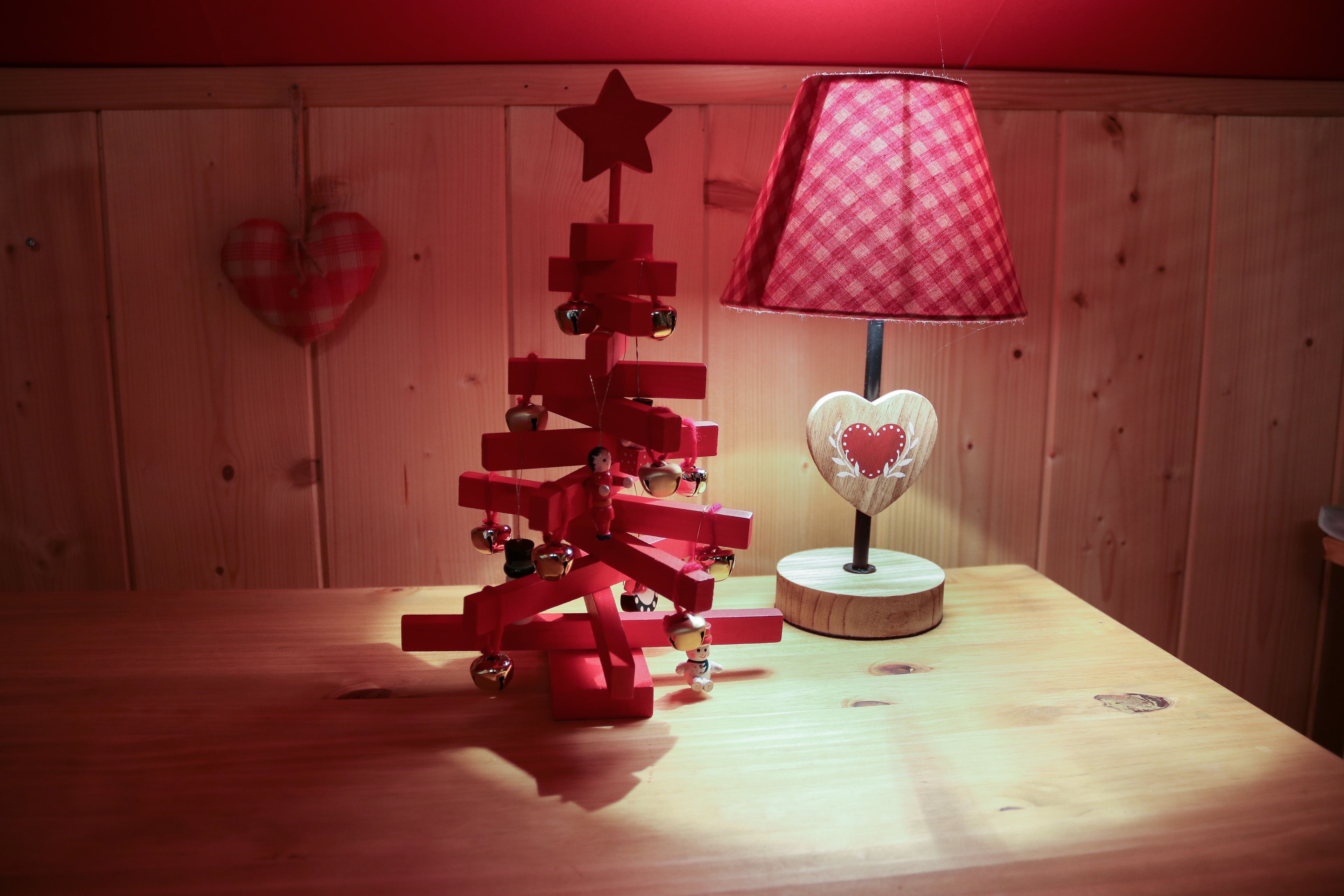 A wooden table with a red and white checkered lamp, a small Christmas tree, and a heart-shaped decoration on the wall.