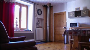 A cozy living room with a wooden floor, a red curtain, a sofa, a dining table with a heart-patterned tablecloth, a microwave, and a wooden cabinet with heart decorations.