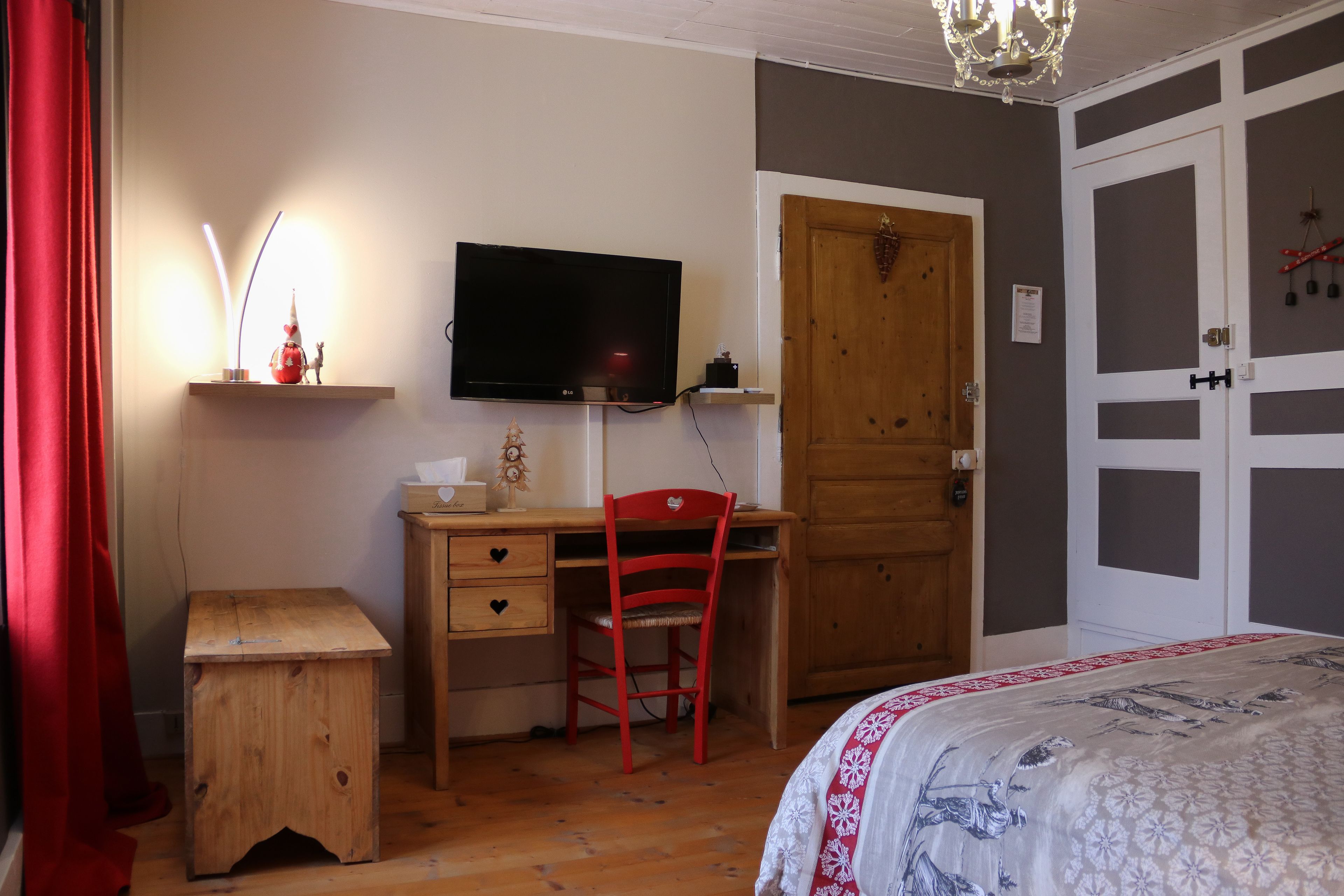 A bedroom with a wooden desk, a red chair, a television, and a bed with a patterned bedspread.