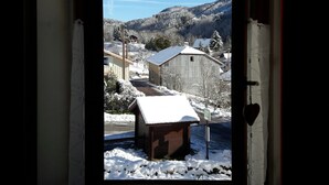 A window view of a snowy landscape with a wooden structure and a mountain in the background.