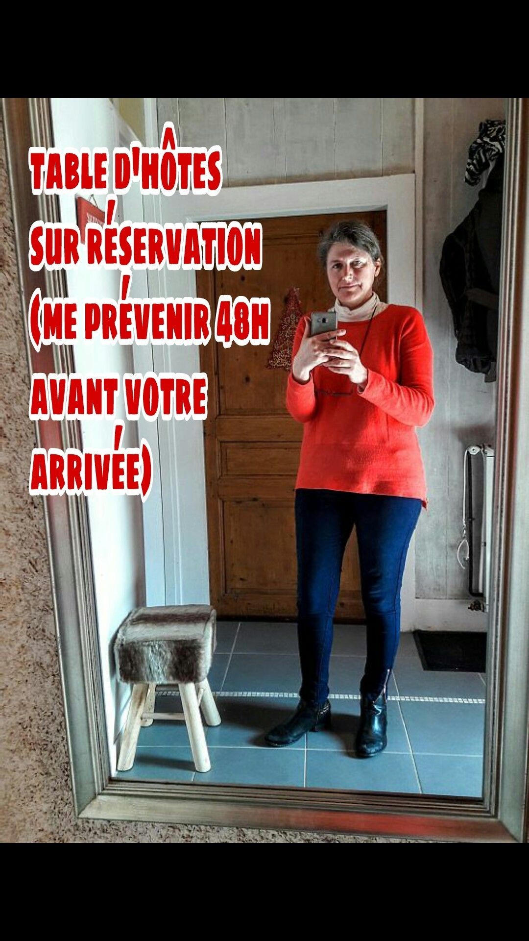 Una persona de pie en un baño, sosteniendo un teléfono, con un espejo que refleja una puerta y un taburete pequeño. Un texto superpuesto indica una reserva de hotel con un aviso de 48 horas.