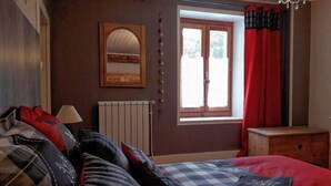 A bedroom with a bed, a radiator, a window with curtains, a mirror, and a chandelier.