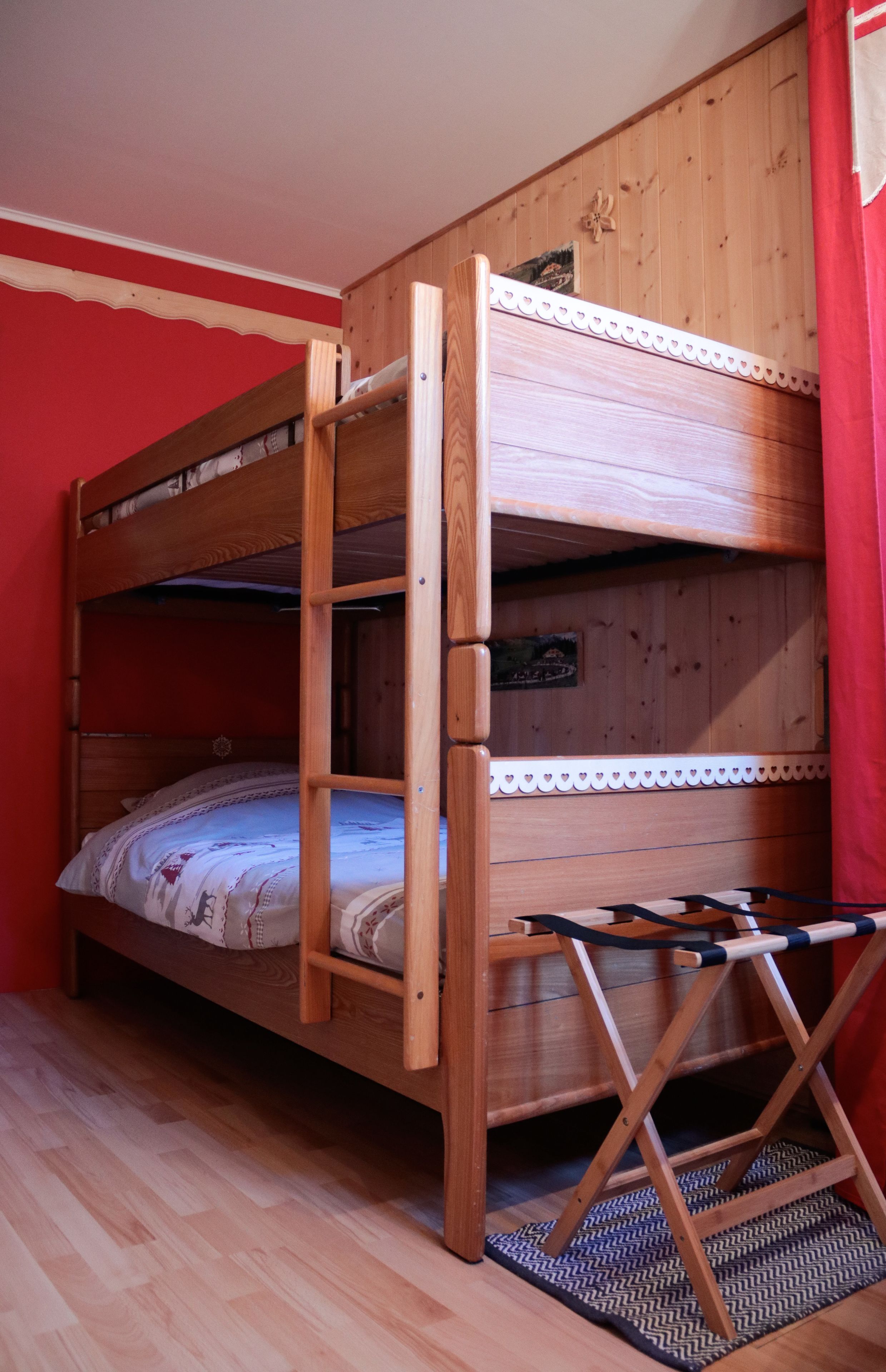 Una cama litera con estructura de madera, un estante pequeño y una escalera.