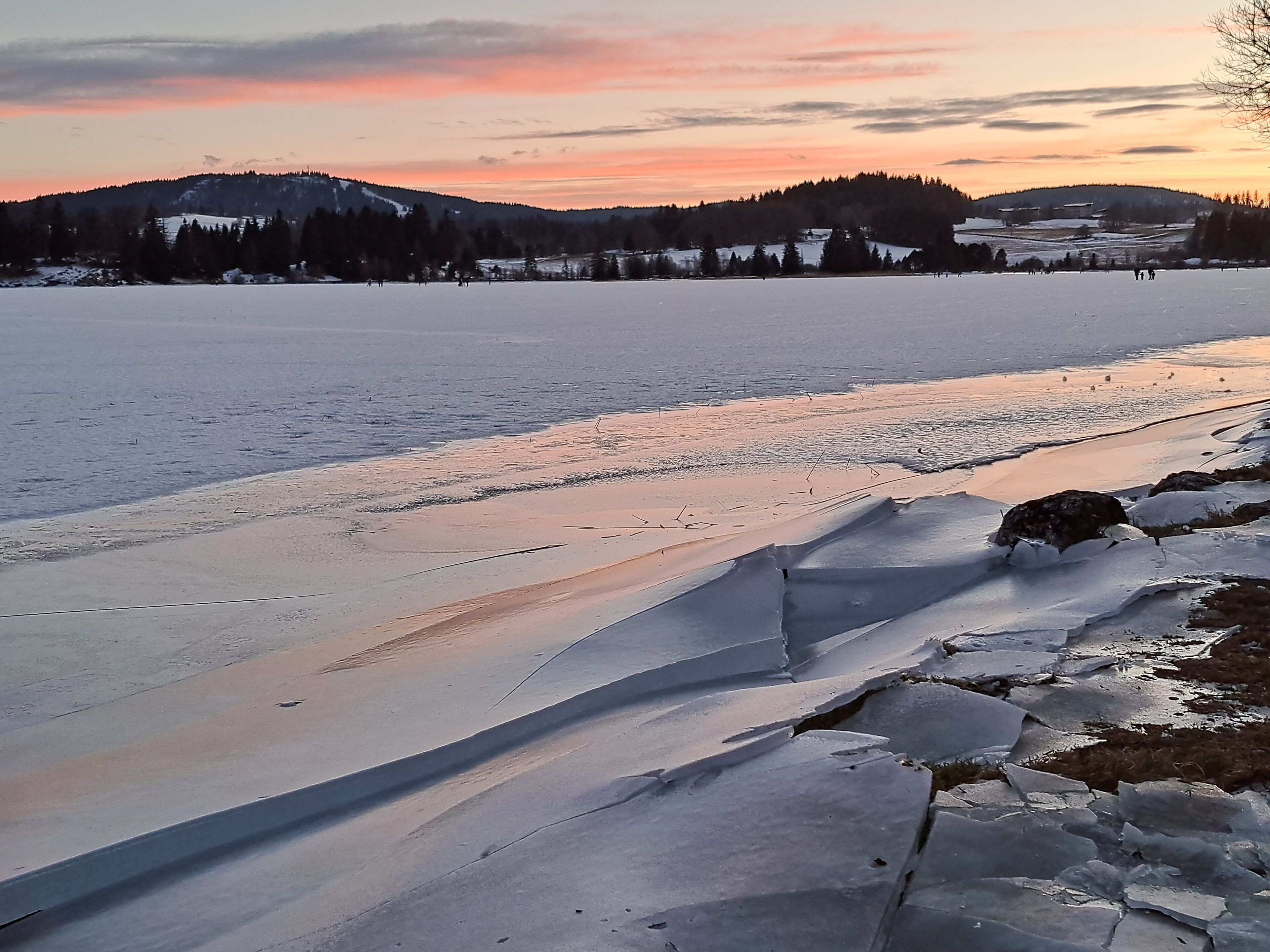A frozen lake with a clear view of the surrounding landscape, including distant hills and a few buildings.
