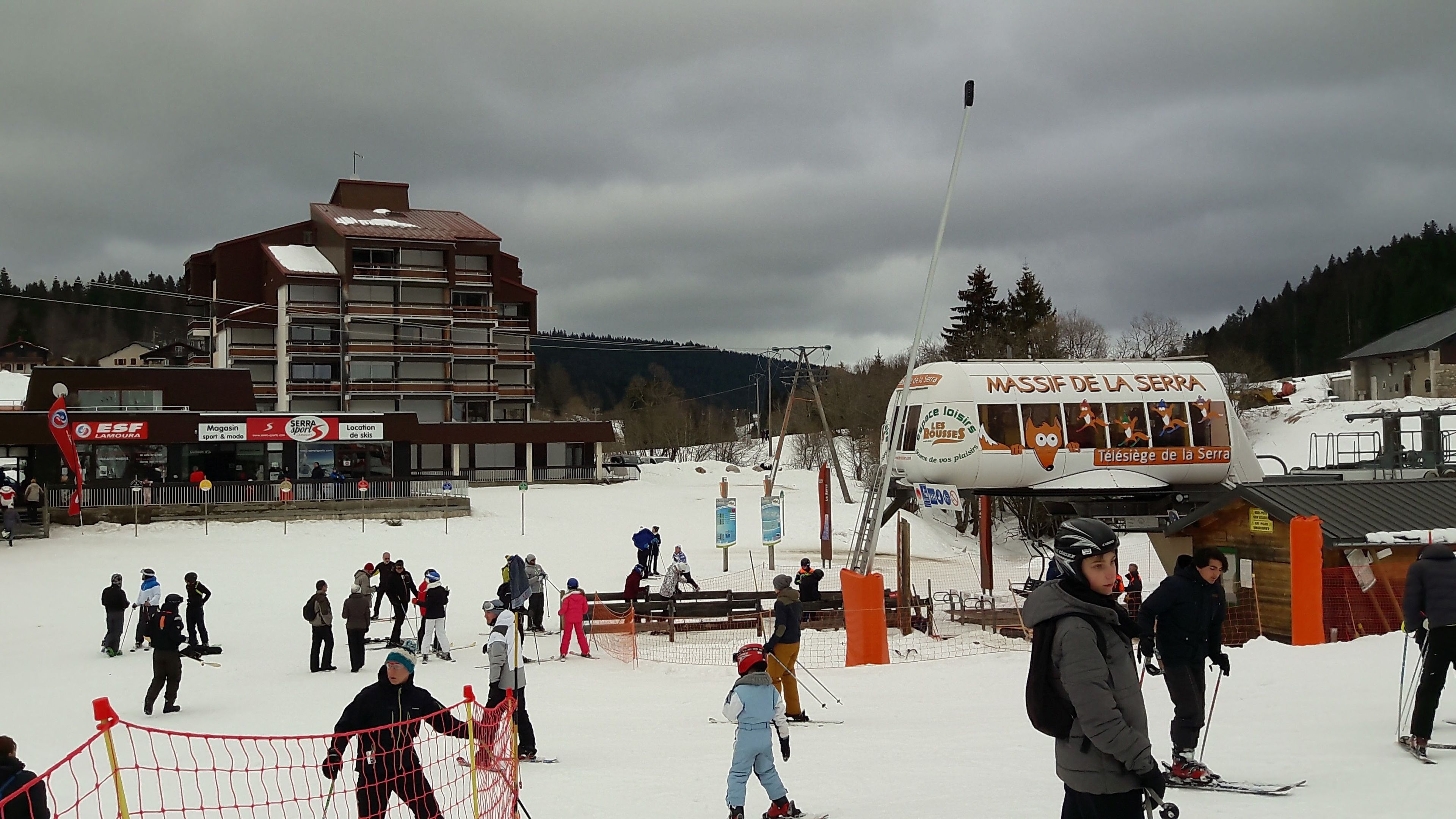 A ski resort with a ski lift, a building with signage, and a snowy landscape.
