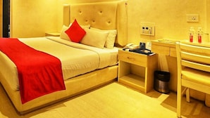 A hotel room with a large bed, bedside table, and a desk with a chair. - Hotel Amrta (Nagpur)