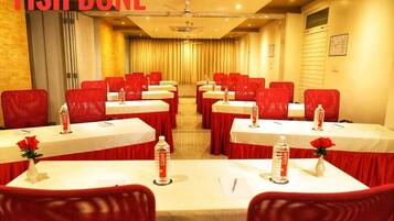 A conference room with red chairs and white tables, each with a bottle of water and a rose vase.