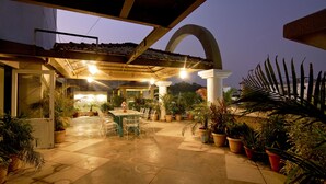 An outdoor patio area with a covered seating area, potted plants, and a table with chairs. - Hotel Amrta (Nagpur)