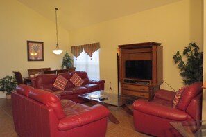 A living room with red leather sofas, a glass coffee table, a wooden entertainment center, and a television. - Deluxe Homes with Private Pool by SVV (Davenport)