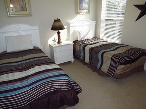A bedroom with two single beds, a nightstand with a lamp, and a window with blinds. - Deluxe Homes with Private Pool by SVV (Davenport)