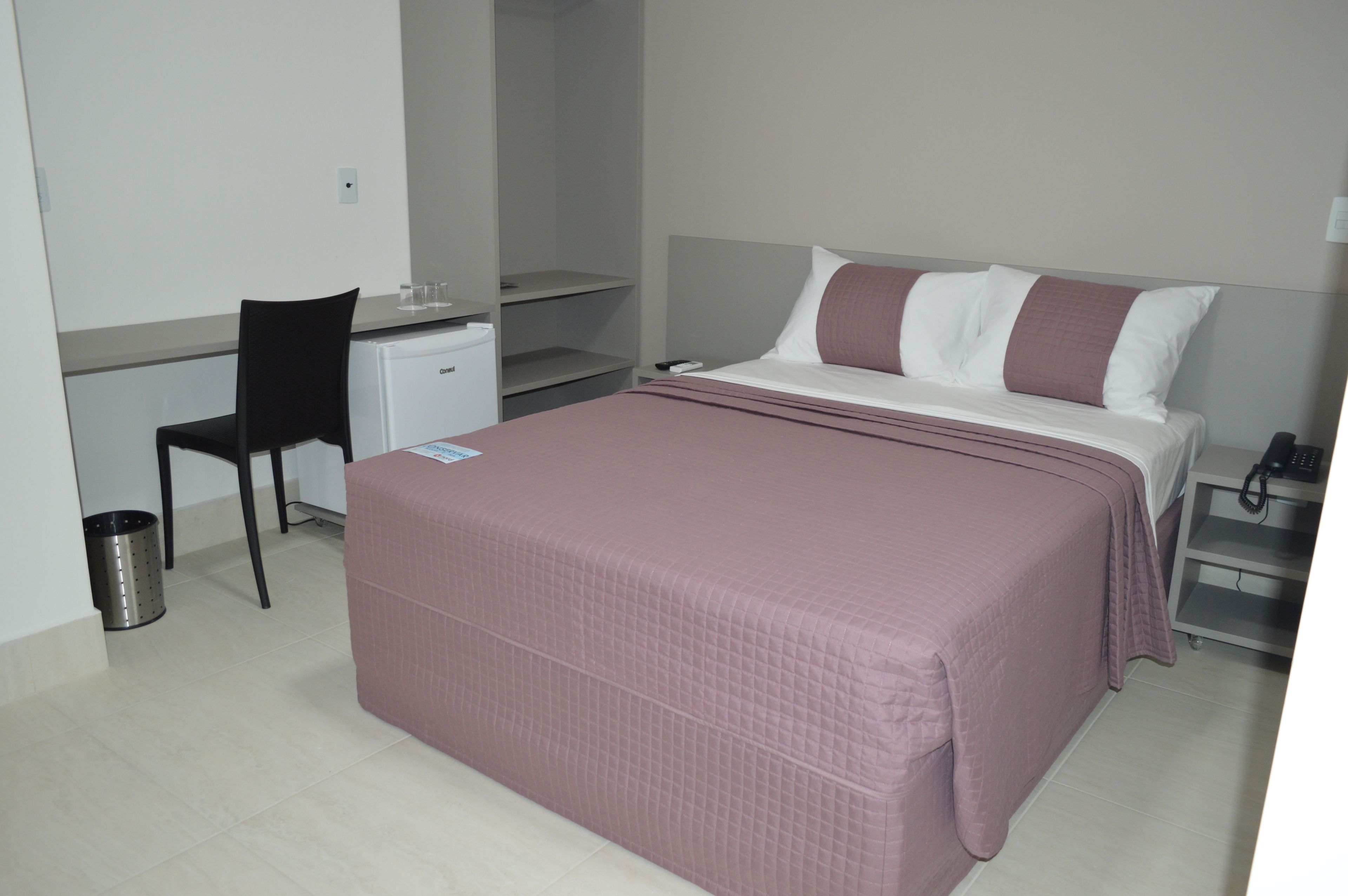 Quarto com cama, escrivaninha, cadeira e lixeira.