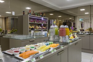 Un bufé con diversos alimentos y bebidas, incluyendo frutas, quesos y una selección de refrescos.