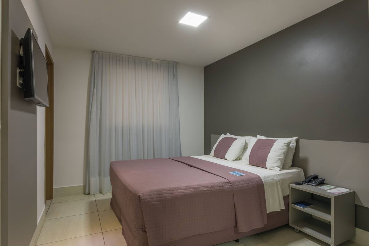 A bedroom with a bed, a nightstand, a TV, and a curtain.