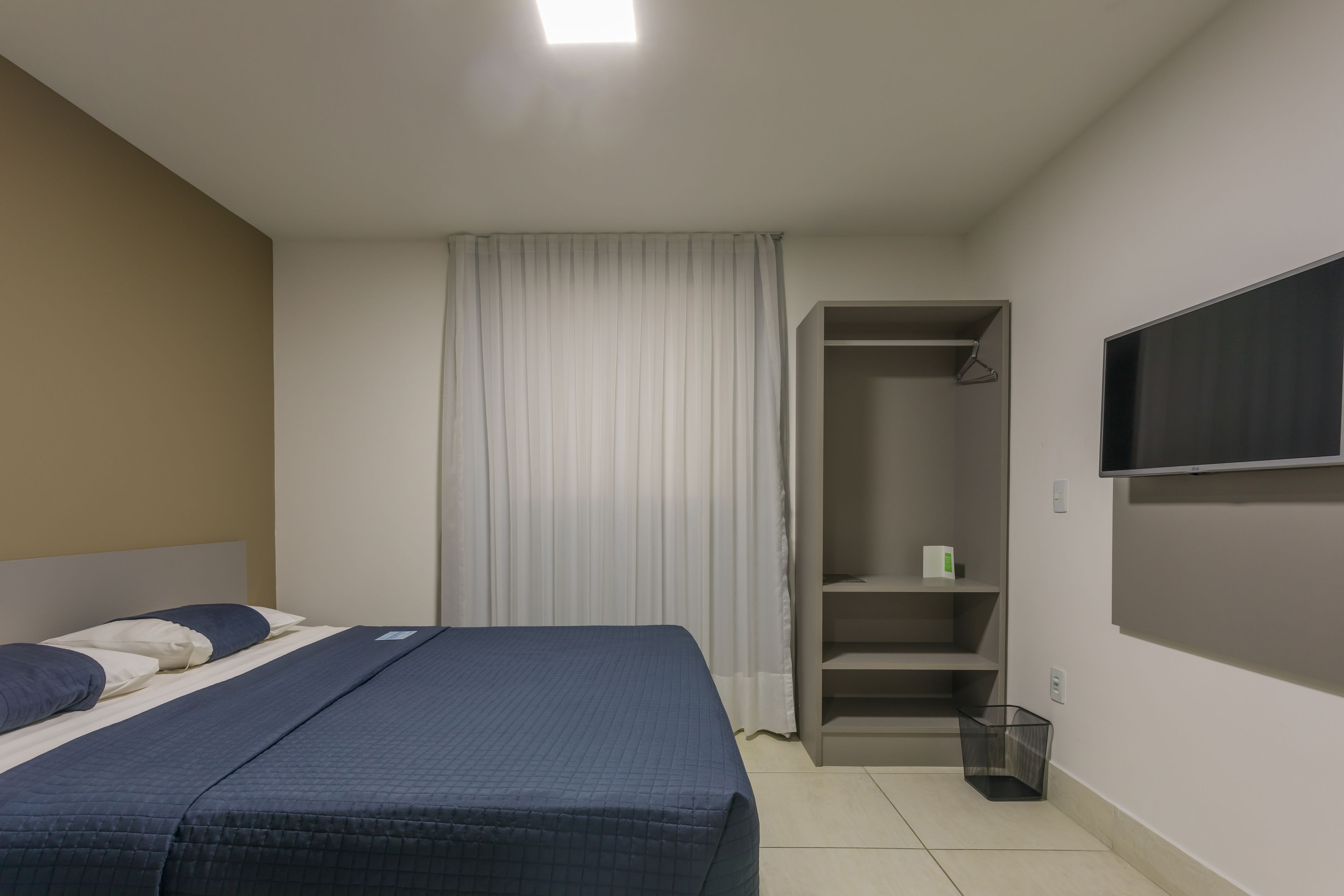 Ein Schlafzimmer mit einem Bett, einem Kleiderschrank, einem Fernseher und einem Vorhang.
