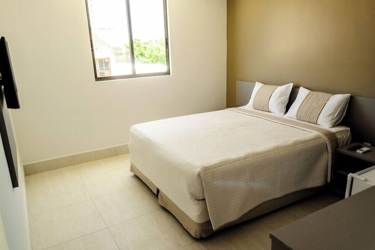 A neatly arranged bedroom with a bed, bedside table, and a window providing natural light.