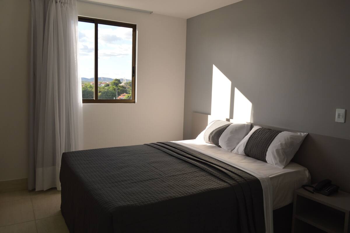 A bedroom with a bed, a nightstand, a window, and a view of the outdoors.