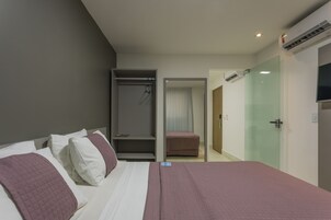 Habitación de hotel con cama, vestidor, puerta de vidrio y aire acondicionado.