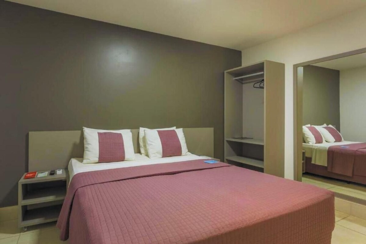 A hotel room with a bed, a nightstand, a wardrobe, and a mirror.