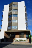 Un edificio moderno de varios pisos con fachada plana, grandes ventanales y una entrada visible con escaleras.