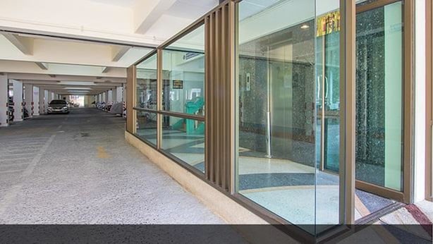 A modern building with a glass facade, a covered parking area, and a visible entrance. - Homeplace Residence (Bangkok)
