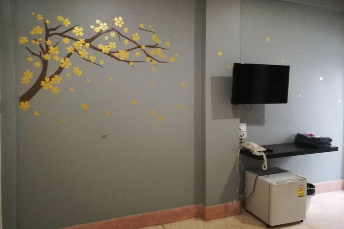 A room with a wall-mounted TV, a small refrigerator, and a shelf with items.