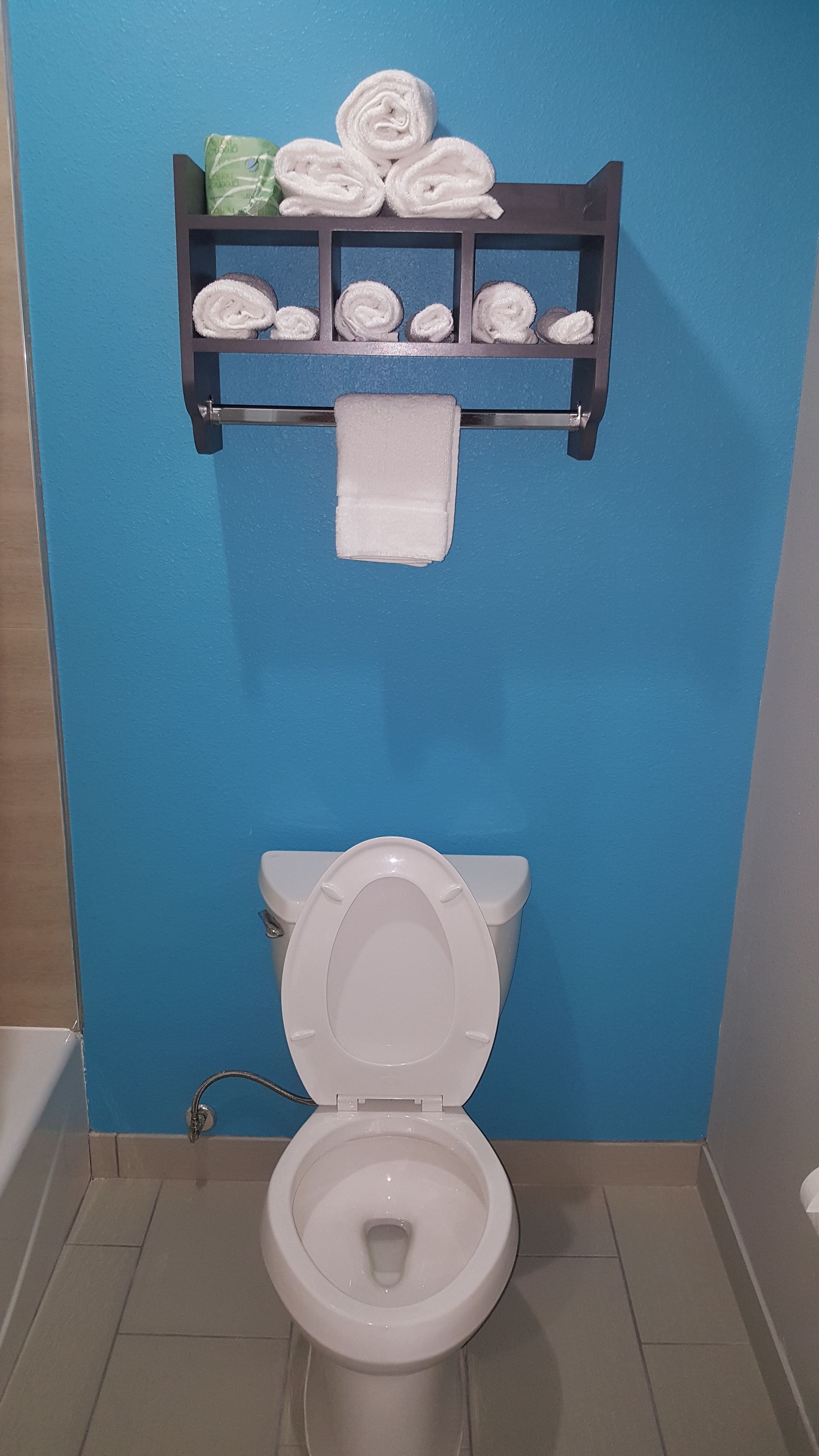 Un baño con una pared azul, un inodoro blanco y un toallero con varias toallas enrolladas.