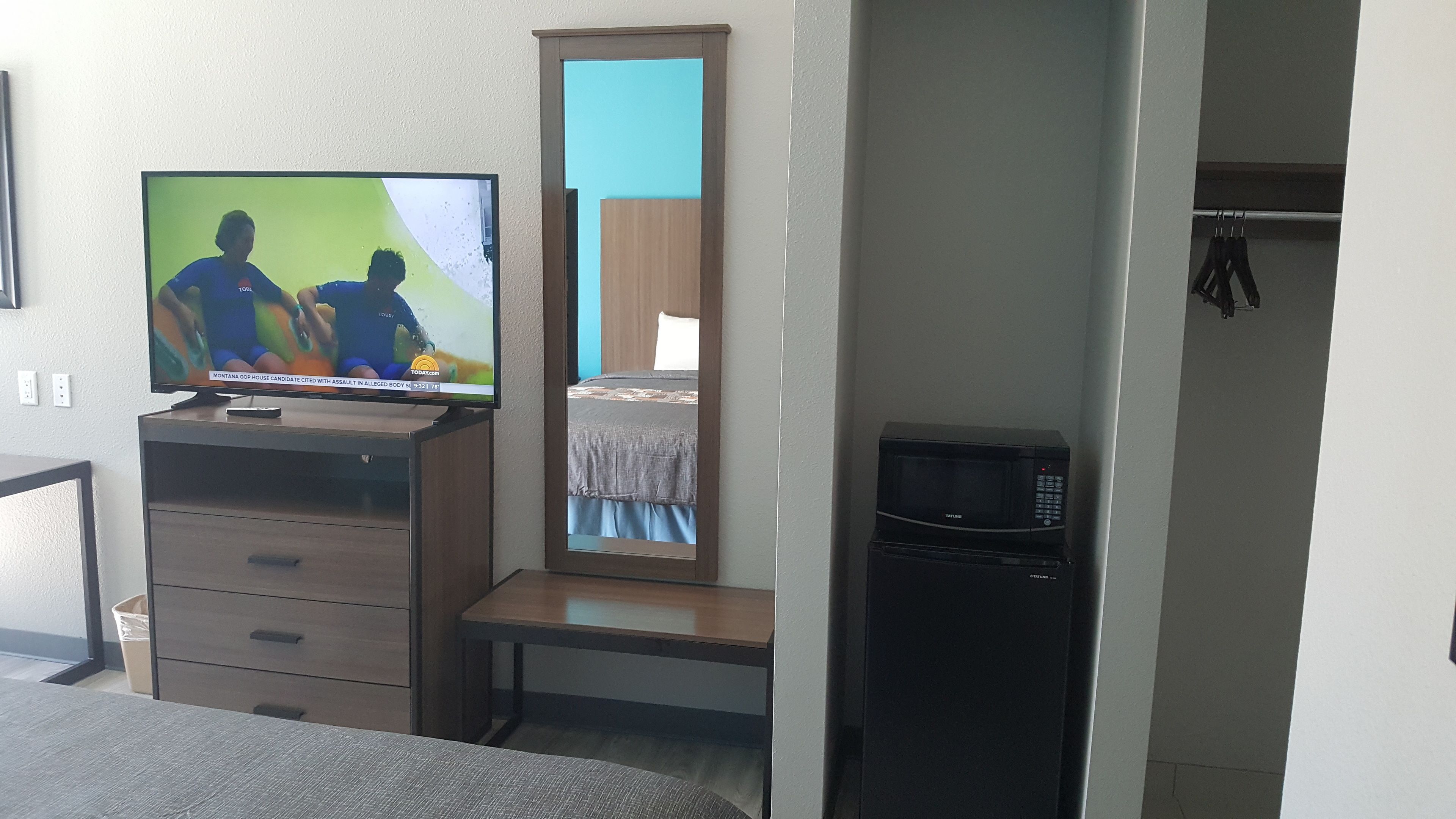 A hotel room with a television on a wooden dresser, a bed with a blue and white bedspread, a microwave, and a small table.