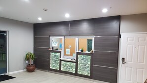 A reception area with a check-in counter, a door, and a potted plant. - Haven Inn & Suites Willowbrook (Houston)
