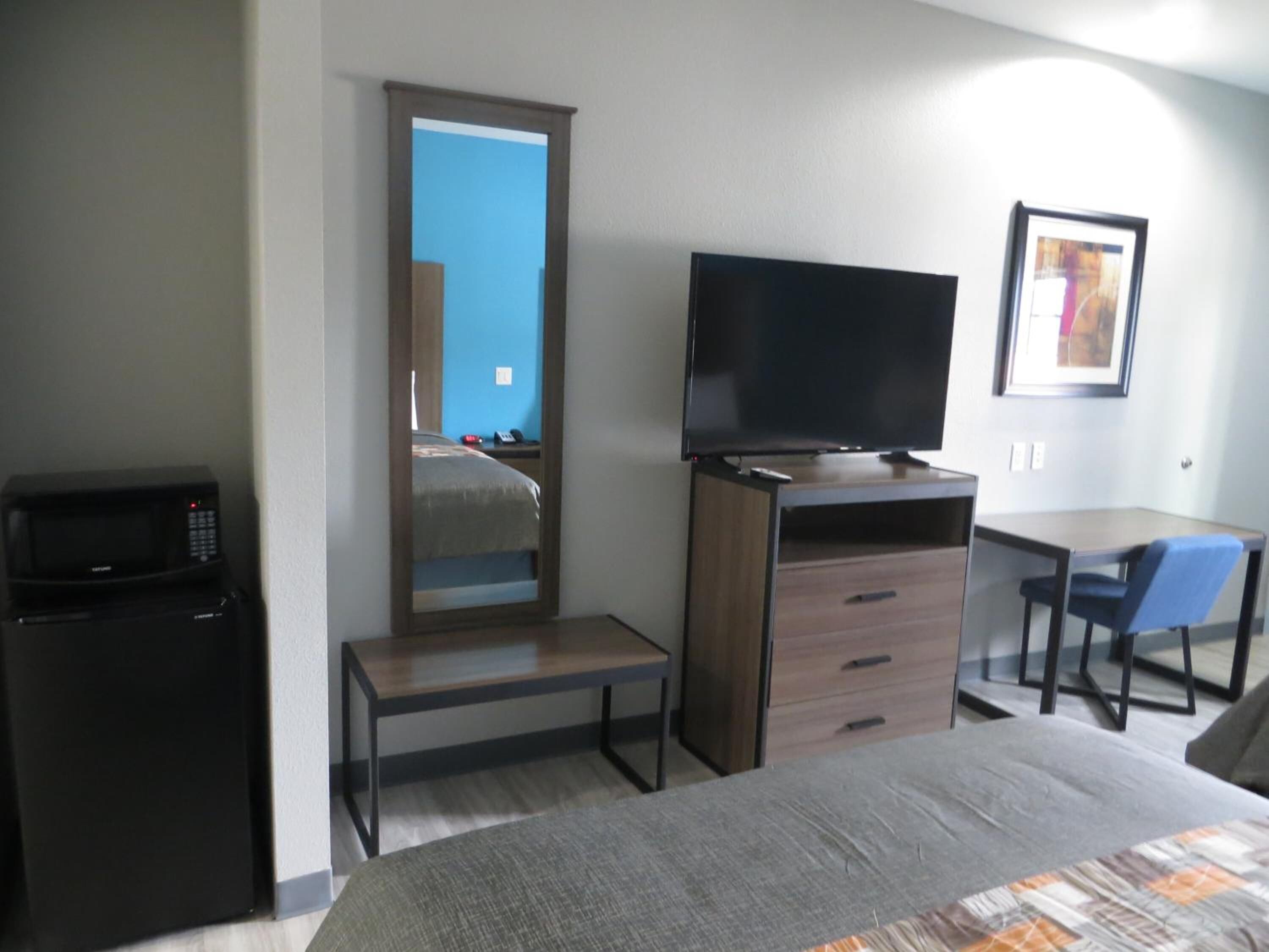 A hotel room with a bed, a desk with a chair, a television, a microwave, and a wardrobe.