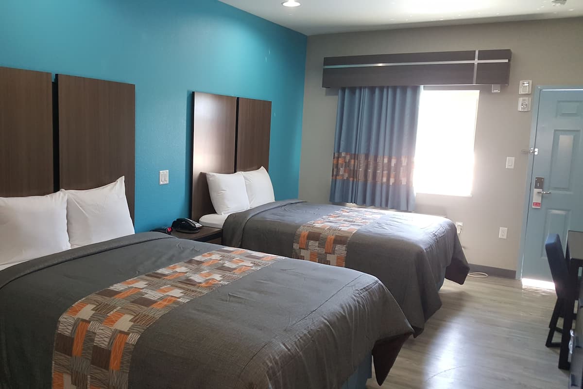A hotel room with two beds, a blue wall, and a window with curtains.