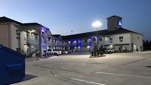 A multi-story hotel with a parking lot, exterior lighting, and a staircase leading to the entrance. - Haven Inn & Suites Willowbrook (Houston)