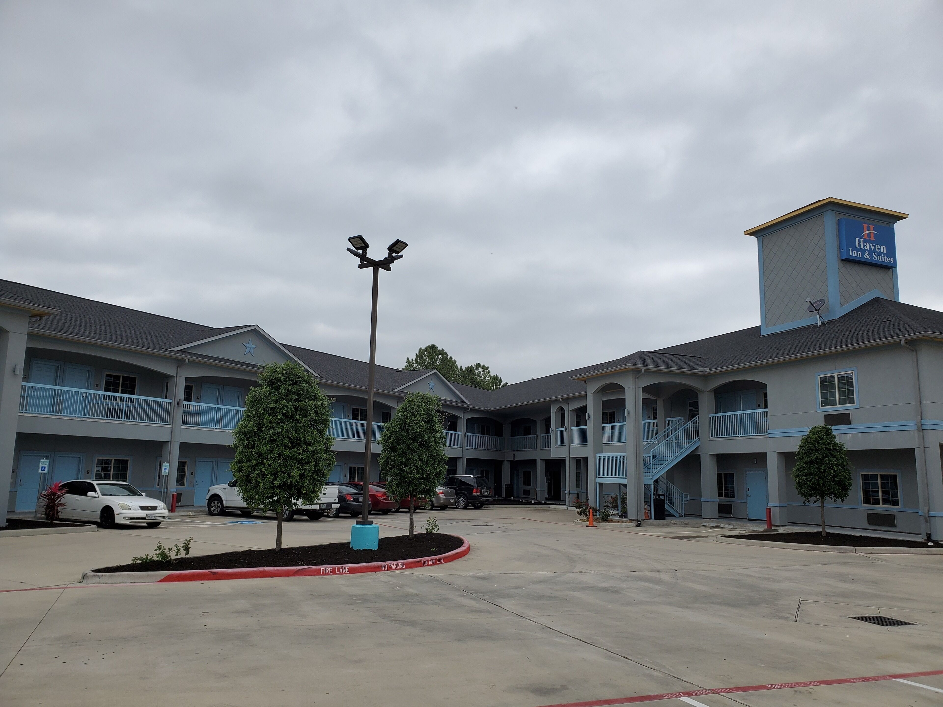 A multi-story hotel with a blue and white exterior, a central courtyard with trees, and a fire lane marked on the ground.