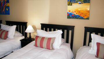 Habitación de hotel con tres camas individuales, cada una con ropa blanca y almohadas a rayas. Hay una mesita de noche con lámpara entre las camas.