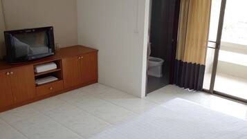 A bedroom with a wooden cabinet, a television, a sliding glass door leading to a bathroom, and a large window with curtains.