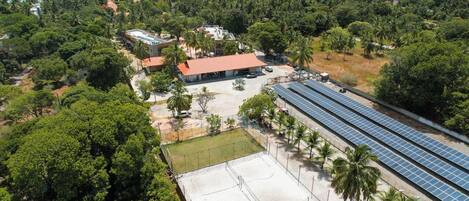 An aerial view of a resort with a large solar panel array, a tennis court, and a beachside location.