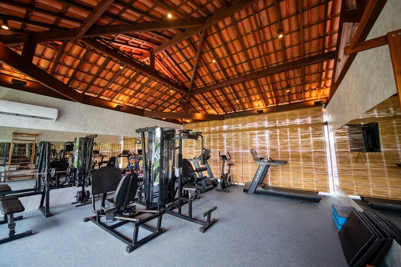 A gym with various exercise equipment, a sloped ceiling, and a wall with vertical blinds.