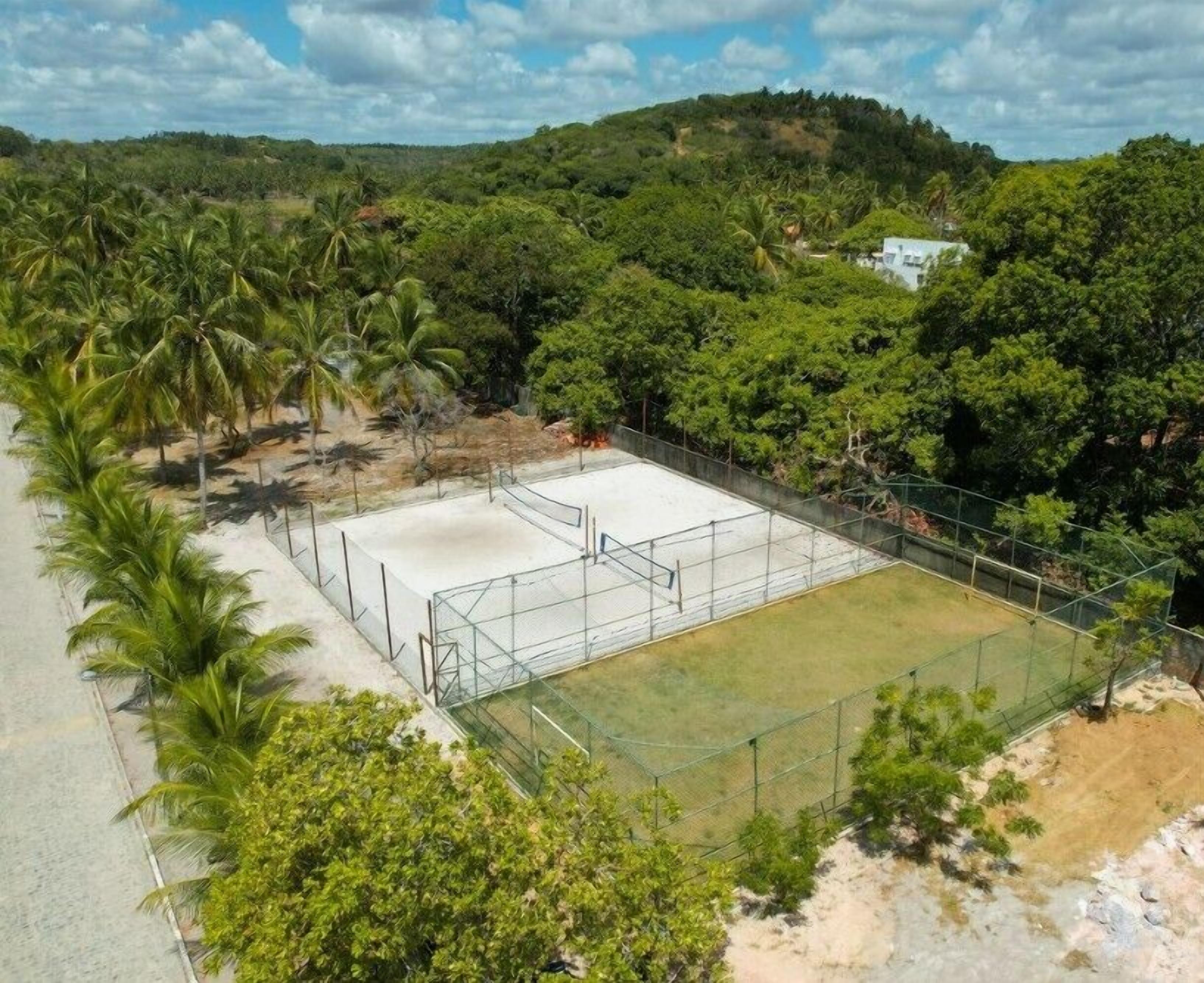 An outdoor tennis court surrounded by lush greenery and hills.