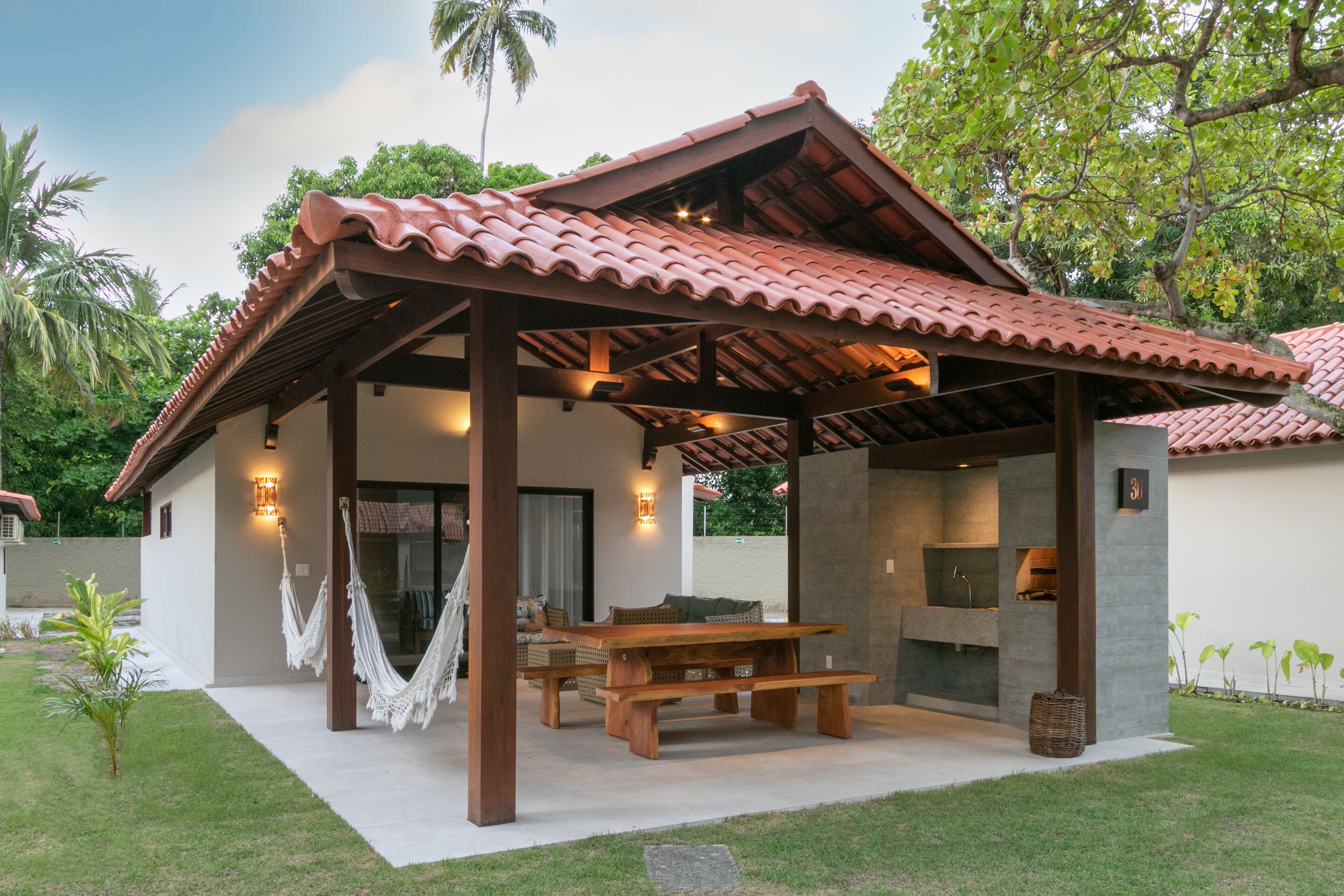 A covered outdoor patio with a wooden table and chairs, a hammock, and a stone fireplace.
