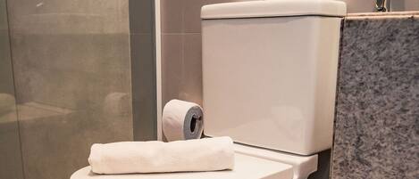 Un baño moderno con inodoro, cubo de basura y encimera de mármol.